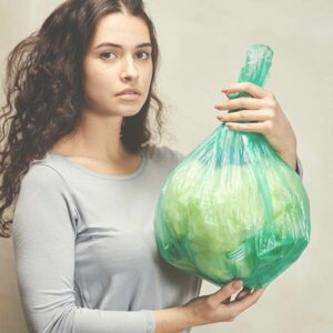 Junge Frau schaut in die Kamera und hält einen Müllsack hoch