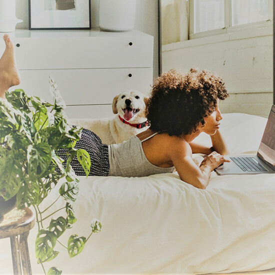 Eine schwarze Frau liegt auf dem Bett und schaut auf ihr Laptop