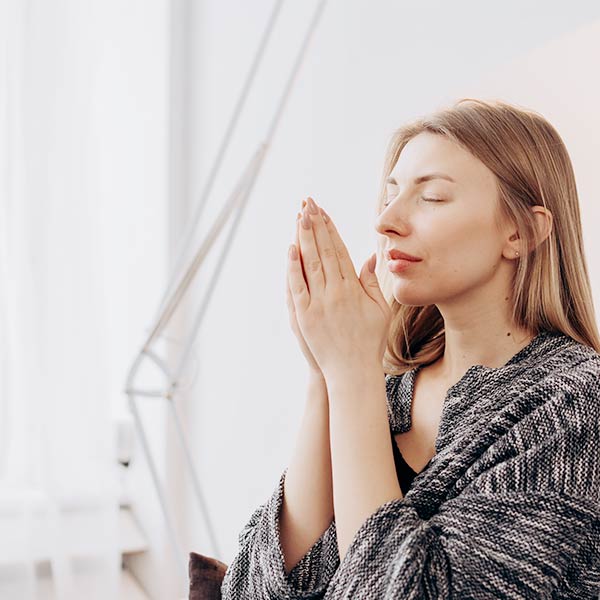 Spirituelle Lebensbegleitung: Junge Frau mit geschlossenen Augen hält sich ihre zusammangelegten Hände vor das Gesicht als würde sie daran riechen