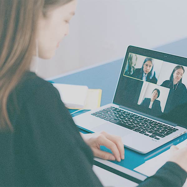 Online-Therapie: Junge Frau sitzt vor enem Laptop, auf dem eine Video-KOnferenz mit mehreren Personen zu sehen ist